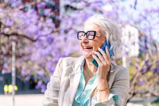 portrait of a lively mature woman laughing happy while talking on mobile phone, concept of technology of communication and modern lifestyle in adulthood, copyspace for text