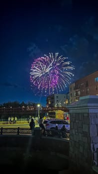 Castle Rock, Colorado, USA-July 4, 2024-A vibrant July 4th fireworks display lights up the night sky, with bright green and gold bursts creating a stunning visual against the dark backdrop. The scene captures the excitement and celebration, with spectators gathered in a suburban area featuring modern buildings and festive lights. The festive atmosphere is palpable as people enjoy the patriotic celebration.