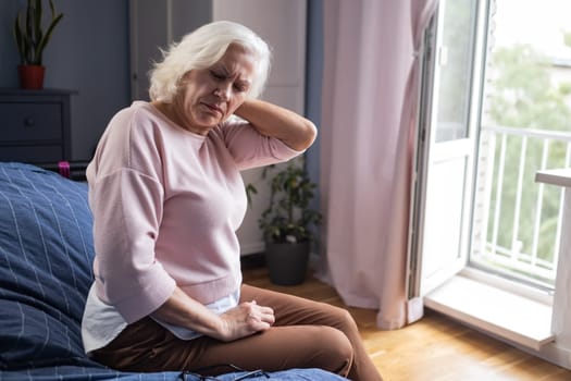 Caucasian senior woman suffering from neck pain sitting at home alone