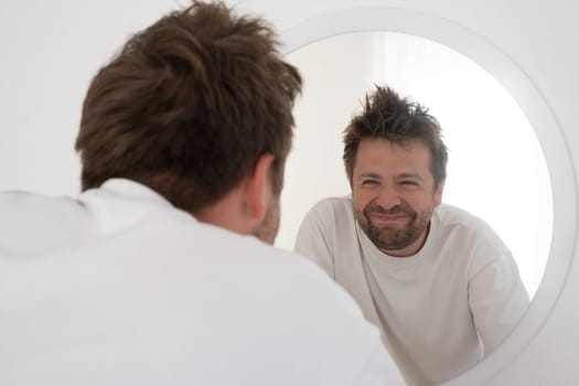 Tired young man is looking at the mirror making funny fces trying to feel better