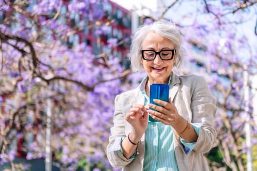 portrait of a lively mature woman smiling happy while typing on mobile phone, concept of technology of communication and modern lifestyle in adulthood, copyspace for text