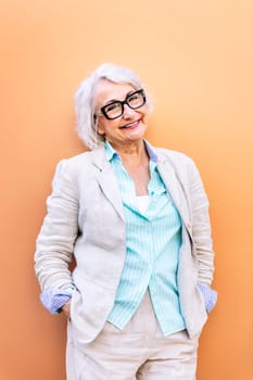 stylish mature woman smiling happy looking at camera leaning on an orange wall, concept of active lifestyle in adulthood, copyspace for text