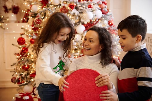Happy family celebrating Christmas together. Mother and children enjoying holiday season with beautifully decorated Christmas tree, festive atmosphere, and gifts encased in warm, cozy surroundings.