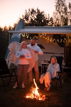 The family is relaxing together by the campfire near their mobile home. Evening family vacation.