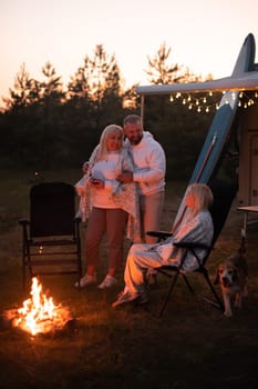 The family is relaxing together by the campfire near their mobile home. Evening family vacation.