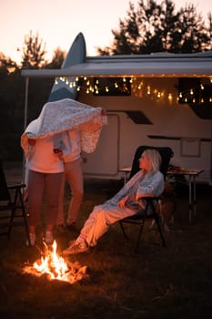 The family rests together in the evening near the campfire and their motorhome.