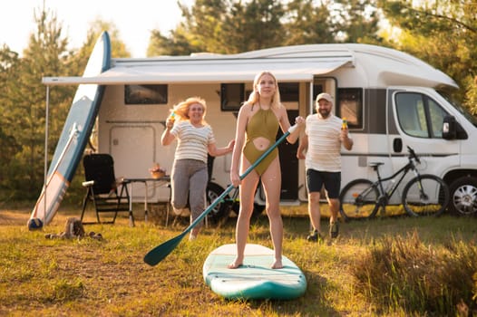 the family is resting next to their mobile home. My daughter is standing with a paddle on a sup board, and her parents pour water on her.