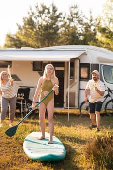 the family is resting next to their mobile home. My daughter is standing with a paddle on a sup board, and her parents pour water on her.