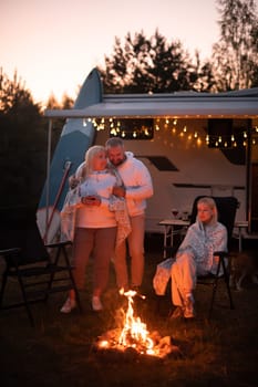 The family is relaxing together by the campfire near their mobile home. Evening family vacation.