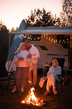 The family is relaxing together by the campfire near their mobile home. Evening family vacation.
