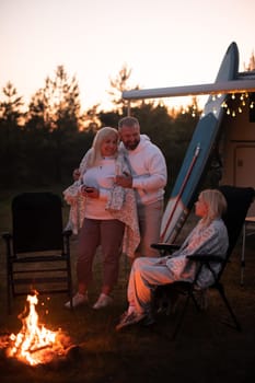 The family is relaxing together by the campfire near their mobile home. Evening family vacation.