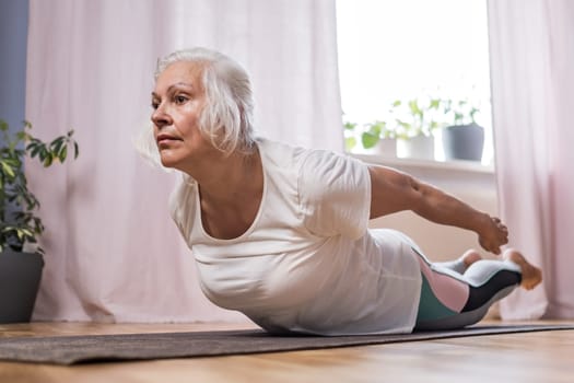 Elderly woman doing pilates on mat in female group at home alone
