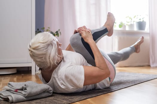 Elderly woman doing pilates on mat in female group at home alone