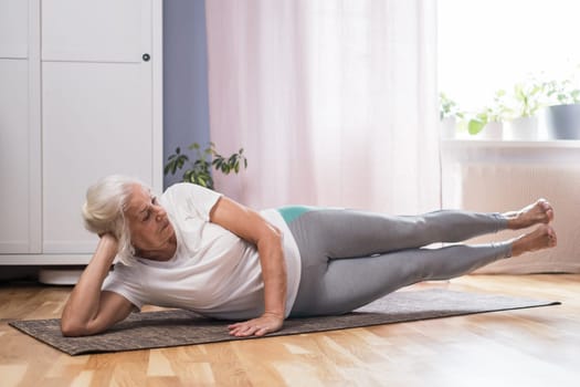 Elderly woman doing pilates on mat in female group at home alone
