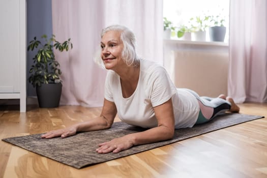 Elderly woman doing pilates on mat in female group at home alone