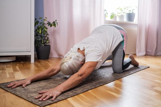 Elderly woman doing pilates on mat in female group at home alone