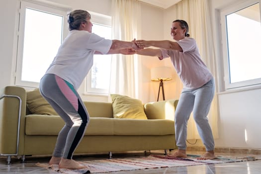 Senior woman exercising at home together with daughter. Active mature woman doing stretching exercise in living room at home.