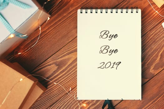 Prepare for Christmas with Notepad and gifts. Notebook with the words Bye Bye 2019 lies on a wooden table. Close up.