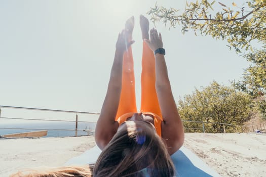 A young woman in orange activewear performs a leg raise exercise on a yoga mat outdoors. She is enjoying the view while working out.