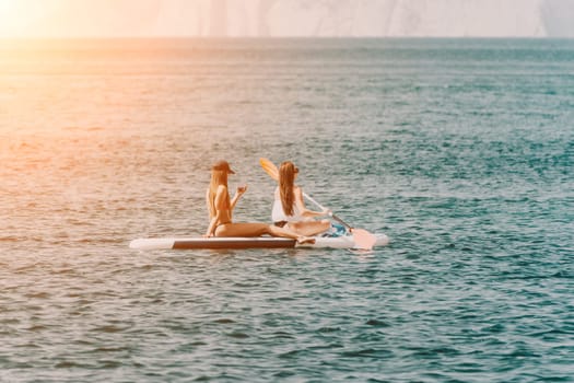 Two women are on a surfboard in the ocean. One of them is wearing a white shirt and the other is wearing a black bikini