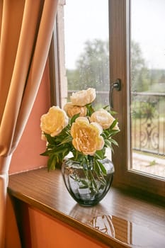 Cream peonies in a glass vase on the window. Flowers at home. Cosiness.