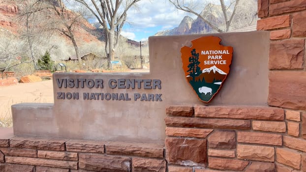 Springdale, Utah, USA – 02.27.2024: Zion National Park sign for the visitor center at Springdale. Zion canyon can be seen in the background.