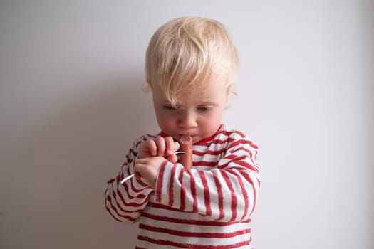 Little happy girl eating tasty sausage on white background.