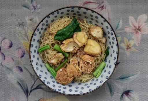 Top view of Egg Noodles with Fried tofu and Chinese kale without Soup sprinkled with Fried garlic in Ceramic bowl. Space for text, Selective focus.