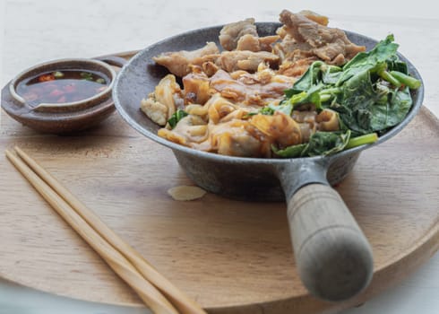 Thai stir-fried Wide Rice Noodles in Sweet Soy Sauce with Pork and Chinese kale ( Pad See-Ew ) served with chopsticks and Thai chilli fish sauce on Round woonden tray. Space for text, Selective focus.