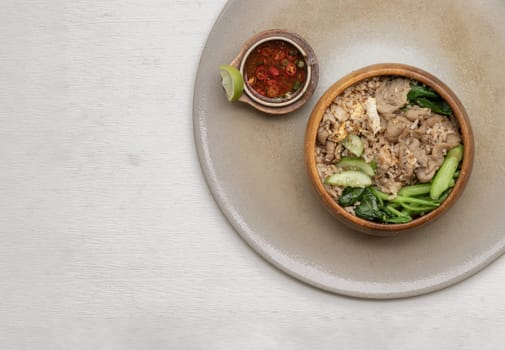 Traditional Egg fried rice with Onion, Fried pork, Chinese kale and Sliced ​​cucumber in Wooden bowl served with Thai chilli fish sauce on ceramic tray. Space for text, Selective focus.