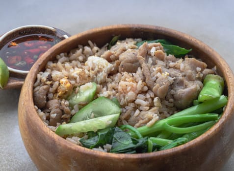 Close-up of Traditional Egg fried rice with Onion, Fried pork, Chinese kale and Sliced ​​cucumber in Wooden bowl served with Thai chilli fish sauce on ceramic tray. Space for text, Selective focus.