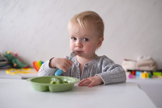 Caucasian little girl eats vegetable salad using fork.