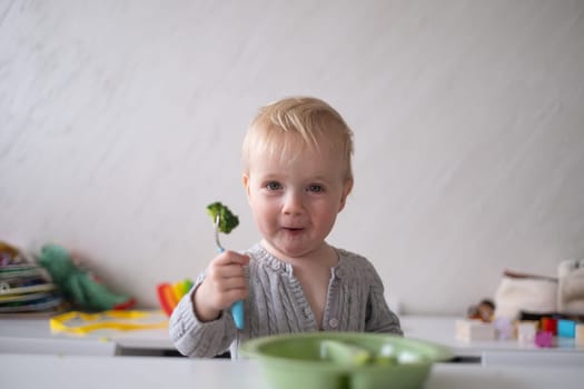 Caucasian little girl eats vegetable salad using fork.