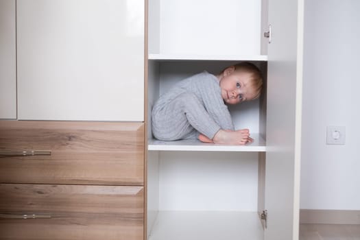happy girl playing hide and seek in wardrobe, Active kid looking out while hiding behind the white door