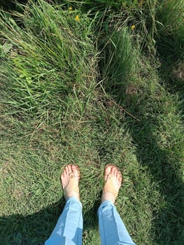 Closeup photo of woman feet in t strap sandal standing on grass during summer. High quality photo. Mobile vertical photo. Summer relax, vacation