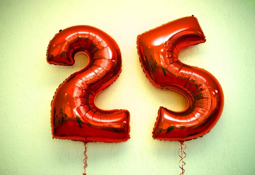 Two shiny red foil balloons shaped as number 25 on white background. Balloons symbolize 25th anniversary. Balloons have reflective surface, creating a festive and celebratory atmosphere.