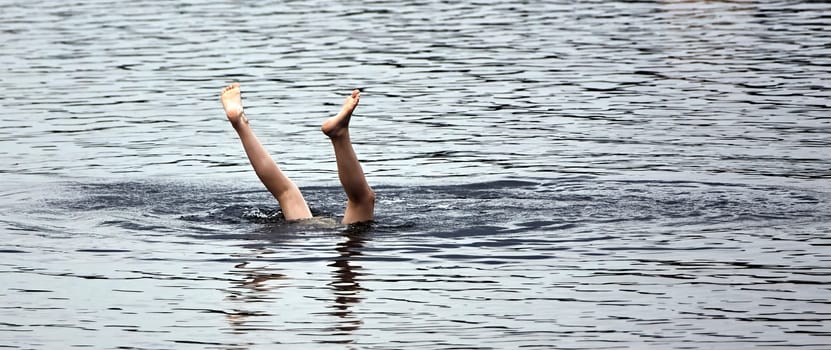 A pair of legs emerge from the water, creating ripples as they break the surface. The sunlight bathes the scene in a warm glow.