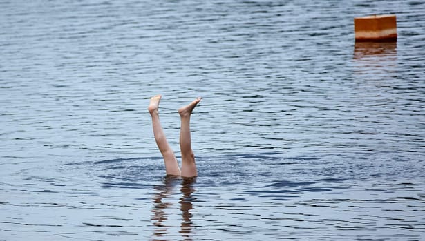 A pair of legs emerge from the water, creating ripples as they break the surface. The sunlight bathes the scene in a warm glow.