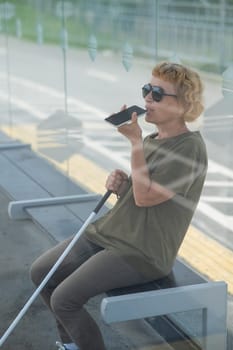 Elderly blind woman sitting at a bus stop and using a smartphone