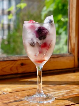 Glass with ice cubes with frozen berries and fruits close-up for a refreshing drink and preservation of seasonal vitamins raspberries, strawberries, cherries, blueberries, mulberries, blackberries