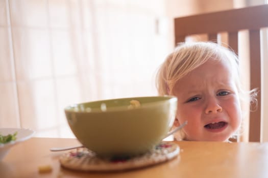 Beautiful blond child eating and crying with tantrum at home.. High quality photo