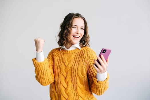A joyful young woman, student or professional, celebrating success with a smartphone in hand. Expressing happiness, isolated against a white background, symbolizing achievement and positive news.