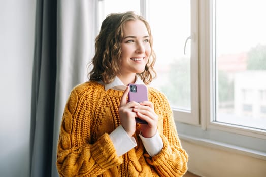 Cheerful Woman Using Smartphone, A close-up shot of a happy, curly-haired woman smiling while browsing the internet on her smartphone. ideal for technology and lifestyle concepts.