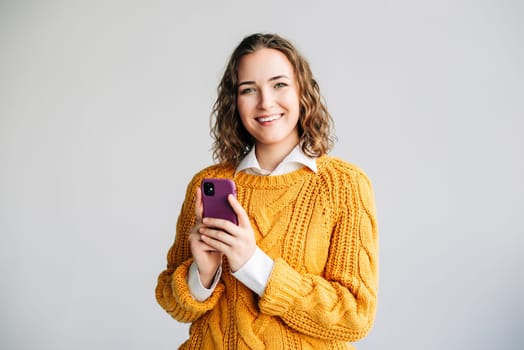 A portrait of a smiling young businesswoman holding a smartphone, engaged in browsing apps, checking online content, and texting messages. Isolated on a white background, professional concept.
