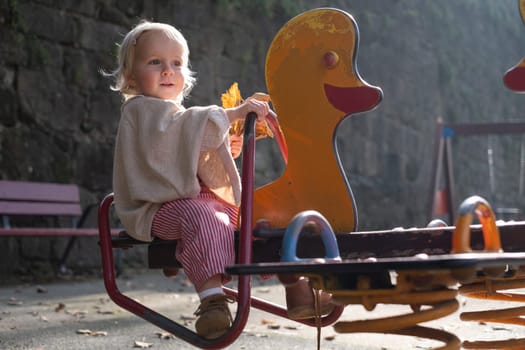 Portrait of a small little cute caucasian girl three years old thinking looking to the ground on the swing in the park