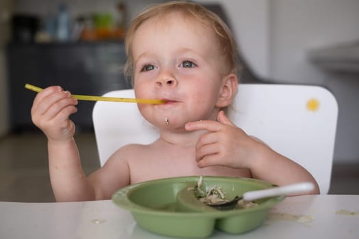 Hungry little kid eating soup with noodles with big spoon. High quality photo