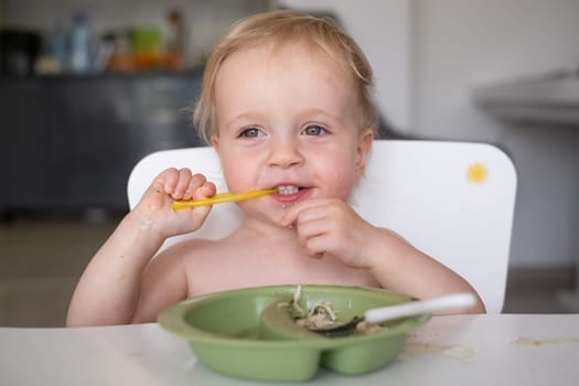 Hungry little kid eating soup with noodles with big spoon. High quality photo