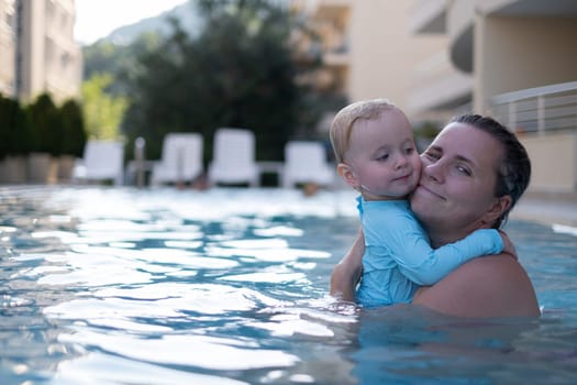 Mother and baby in outdoor swimming pool of tropical resort. Kid learning to swim. Mom and child playing in water. Family summer vacation in exotic destination. Active and healthy sport for kids.