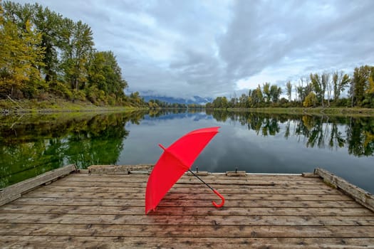 A concept photo of a red umbrella resting on a wooden dock by Kootenai RIver in north Idaho during autumn.