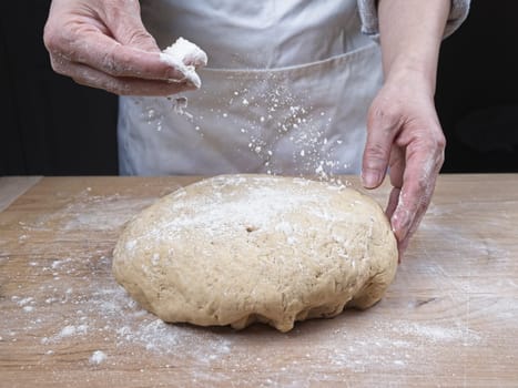 A close up studio photo of a woman's hands throwing flour onto a ball of dough on a cutting board.